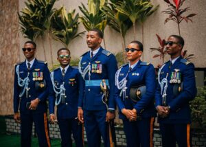 Five African military officers in decorated uniforms posing outdoors with plants.